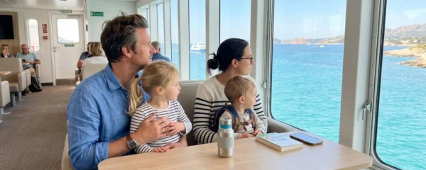 Une famille avec deux jeunes enfants assise dans un salon panoramique de ferry moderne, regardant la mer Méditerranée à travers de grandes baies vitrées