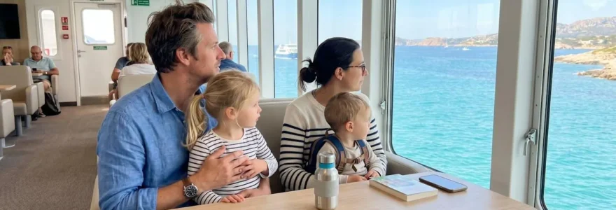 Une famille avec deux jeunes enfants assise dans un salon panoramique de ferry moderne, regardant la mer Méditerranée à travers de grandes baies vitrées